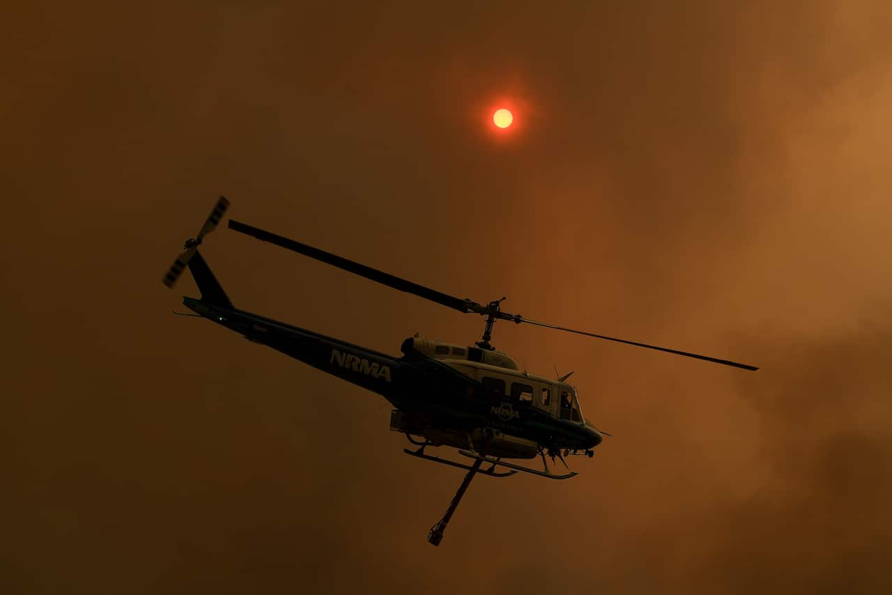 A firefighting helicopter is seen as the Gospers Mountain Fire impacts property at Bilpin.
