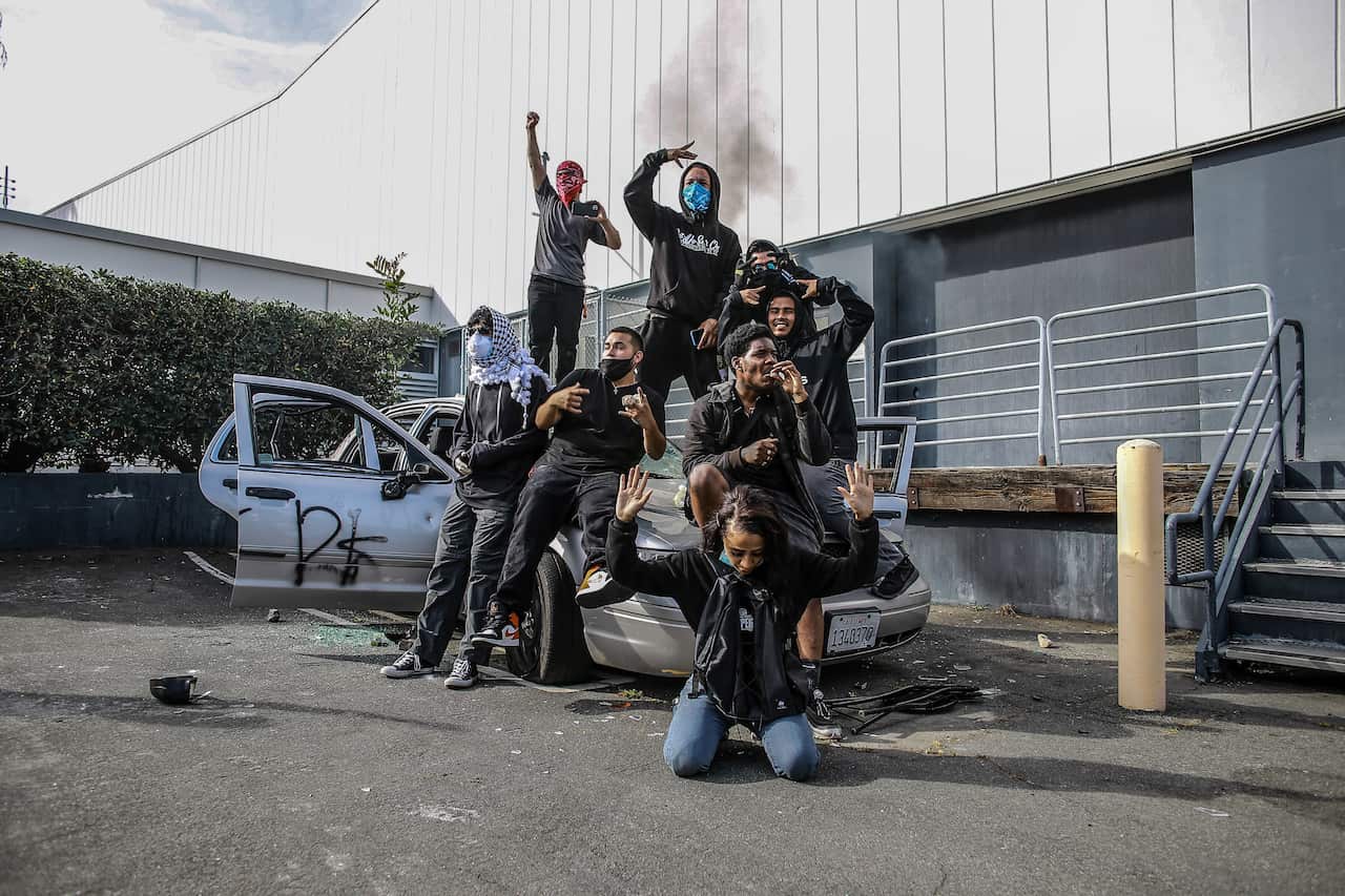 Protesters pose for a photograph on top of a destroyed car before setting it on fire during a protest in LA.