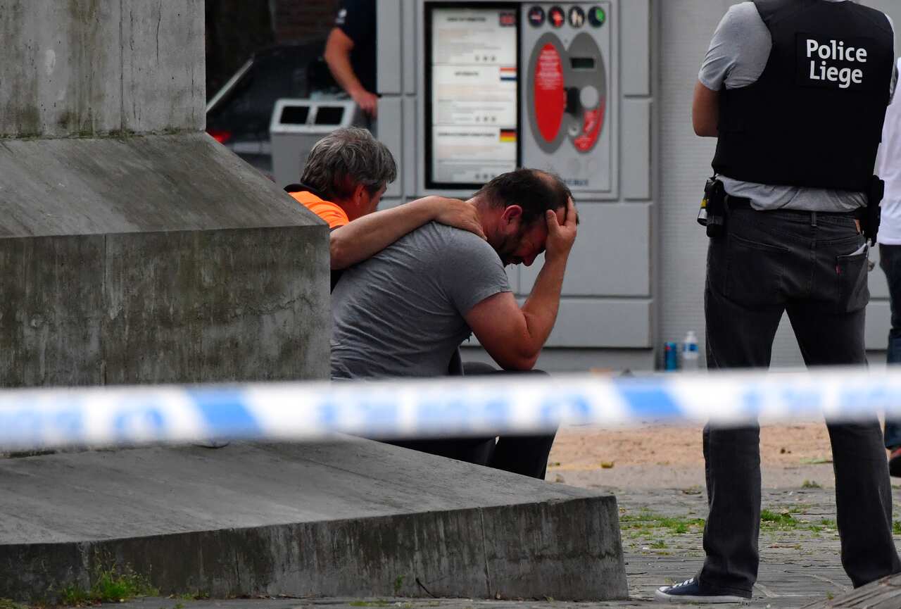 A police man stands next to a man who holds his head in his hands at the scene of a shooting in Liege, Belgium, Tuesday, May 29, 2018.
