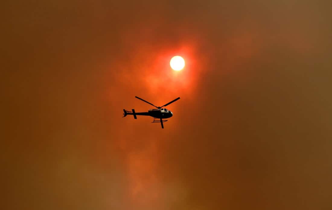 A spotter helicopter flies through thick bushfire smoke in Nana Glen, near Coffs Harbour, Tuesday, 12 November, 2019.