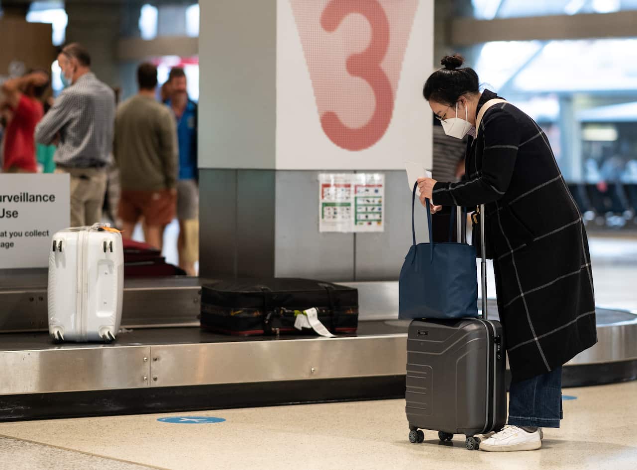 Passengers wearing face masks collect their baggage.