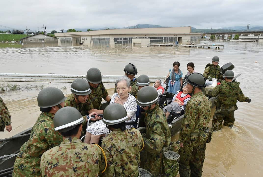 Army personnel carry people rescued from isolated nursing home in Kurashiki.