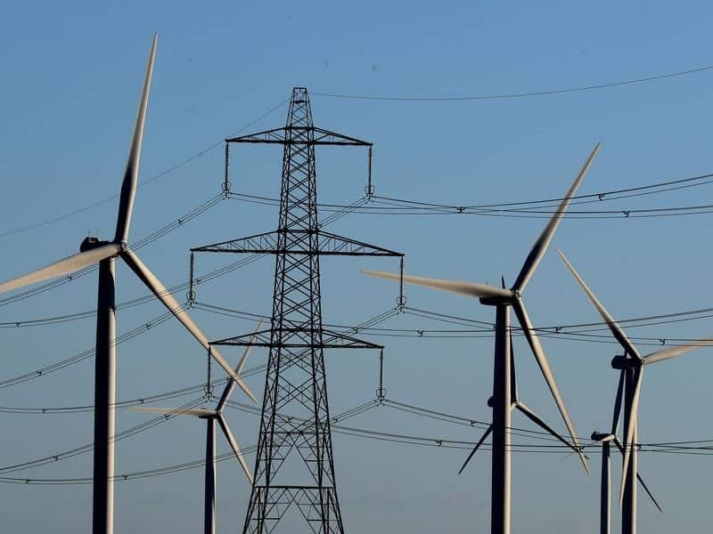 A view of a wind farm amongst electricity pylon.