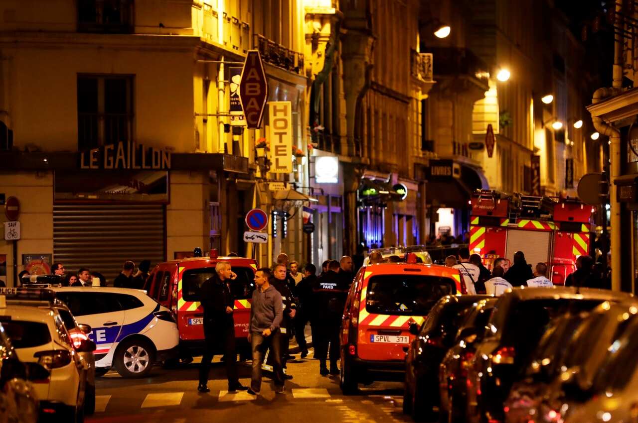 Policemen and emergency service members stand in a blocked street in Paris centre after one person was killed and several injured