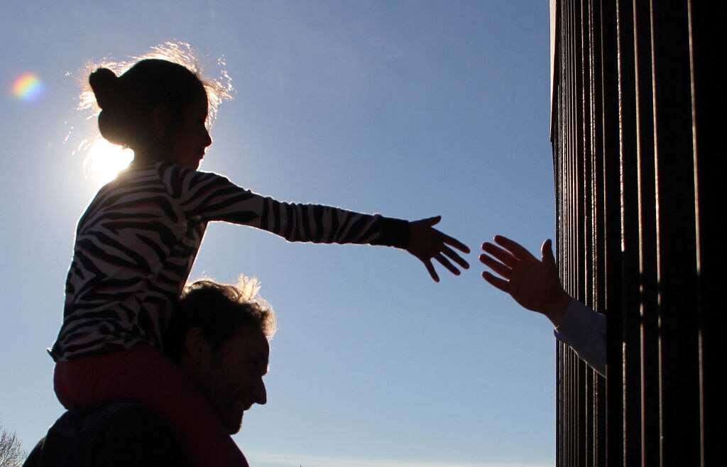 A girl from a neighbourhood near Ciudad Juarez in Mexico touches hands with a person on the US through the border fence.