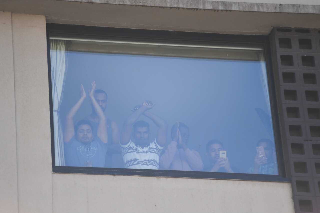 Refugees inside the Park Hotel in Melbourne gesture to protesters outside.