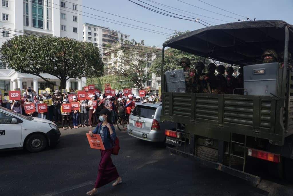 Protesters hold up signs during a demonstration against the military coup next to a truck carrying soldiers outside the Central Bank of Myanmar in Yangon on 15 February 2021.
