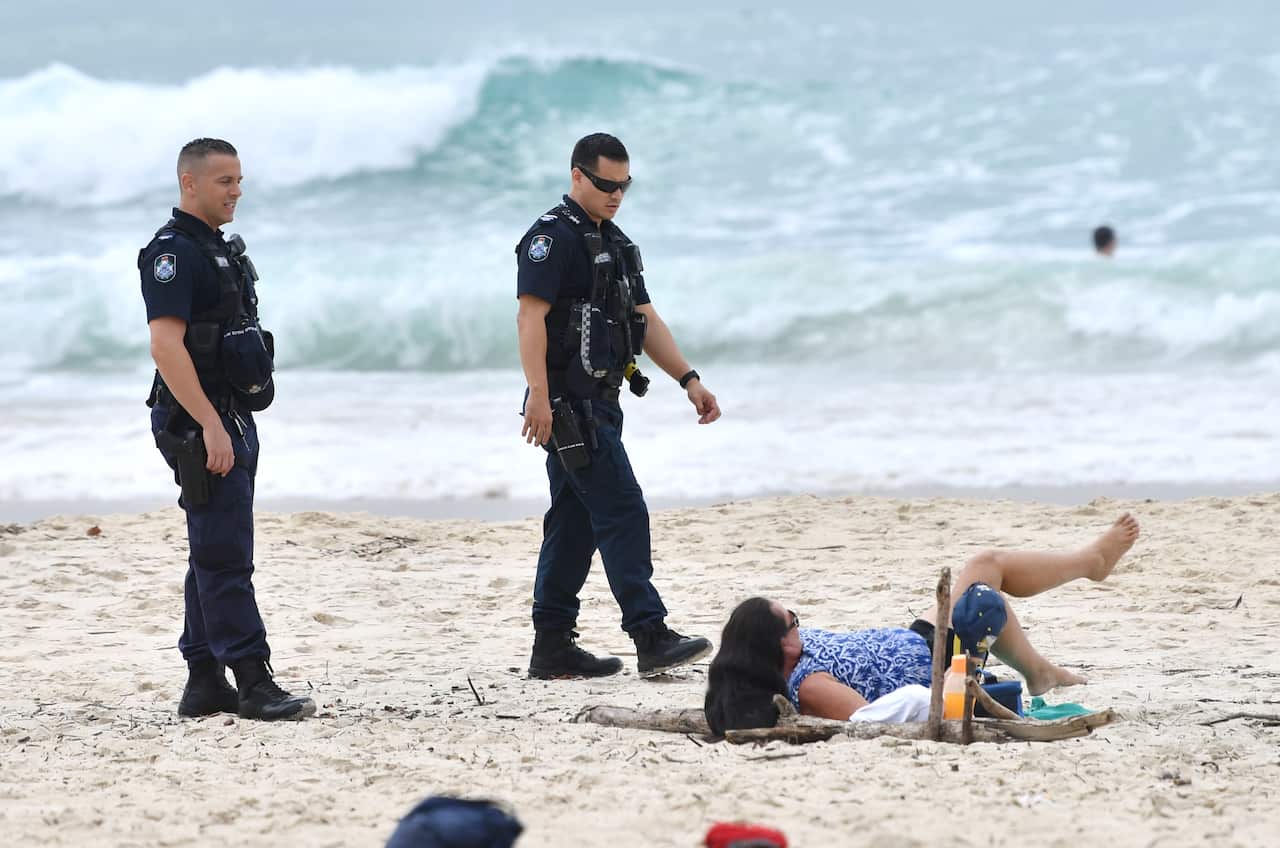 Queensland Police are seen moving on a sunbather from the beach at Burleigh Heads on the Gold Coast.