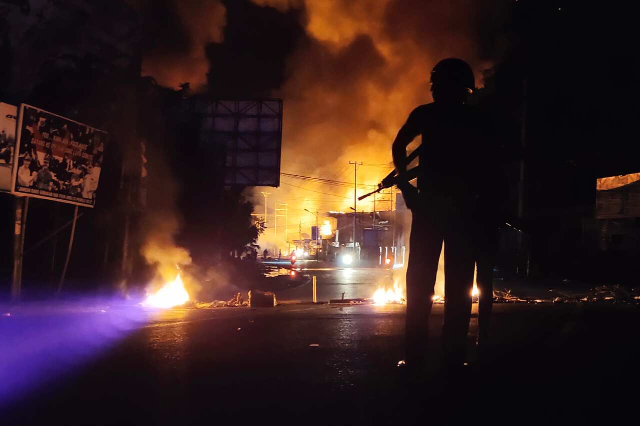 An armed Indonesian policeman stands guard near a burning building after hundreds of demonstrators marched near Papua's biggest city Jayapura.