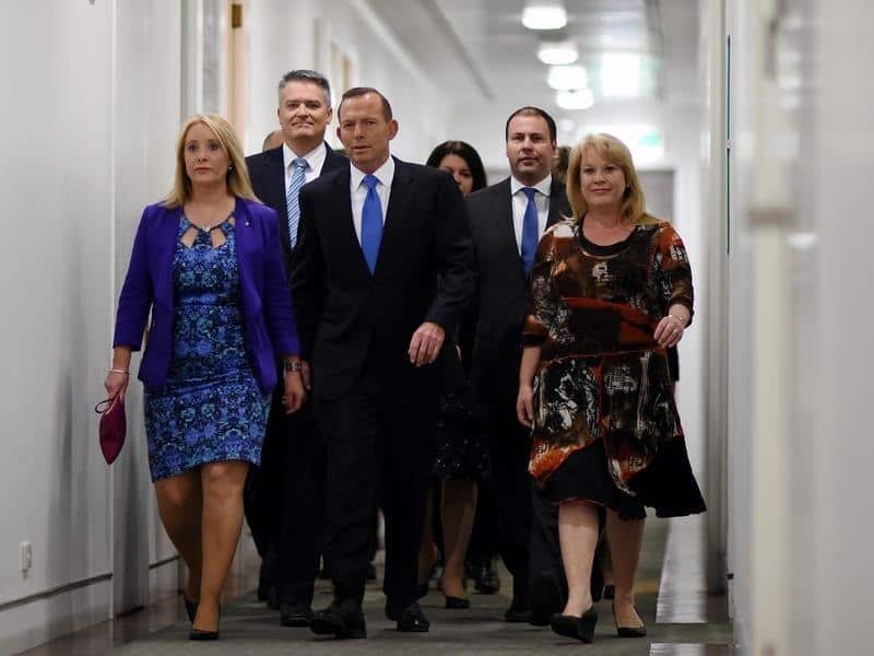 Prime Minister Tony Abbott arrives surrounded by fellow MPs.