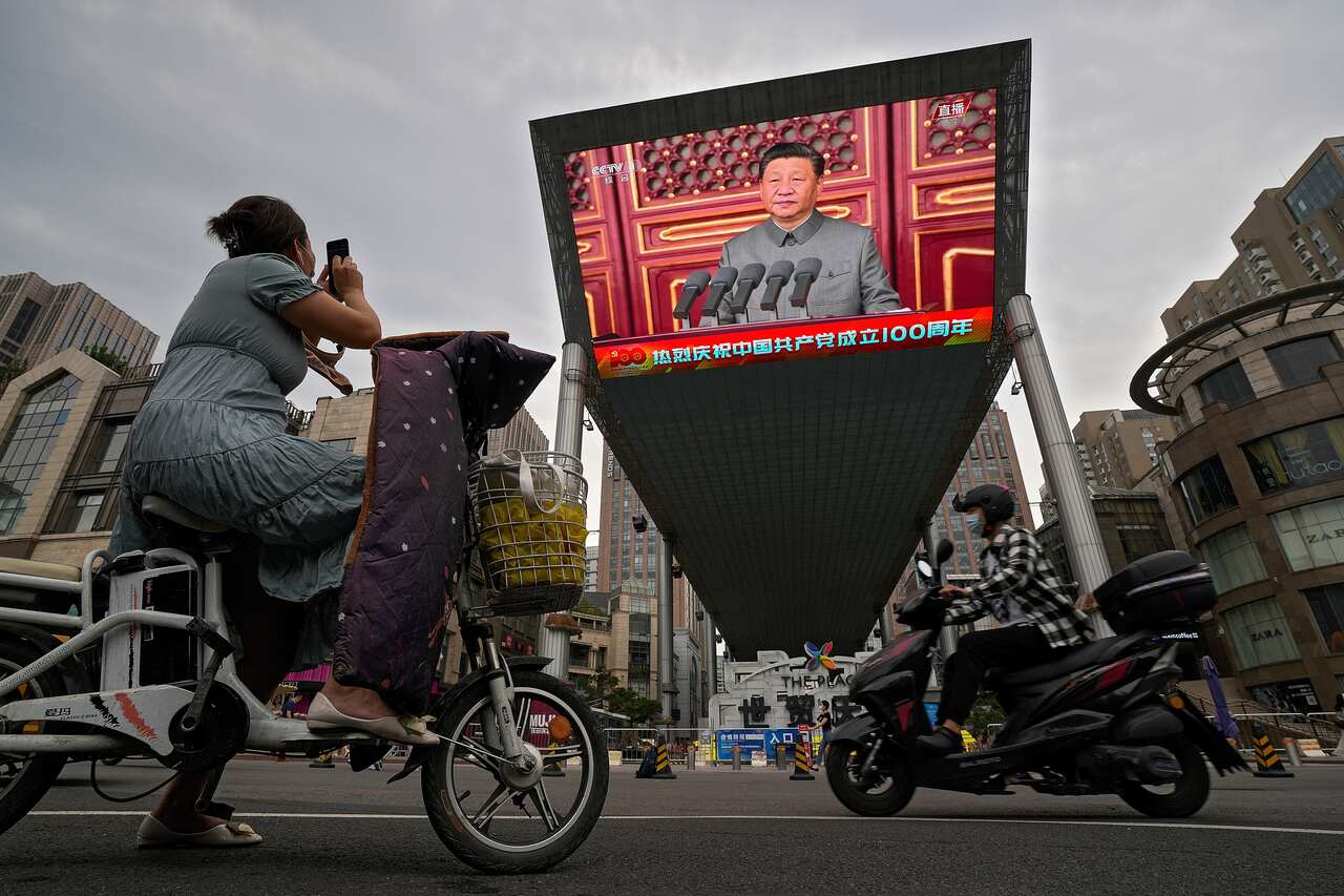 A woman films a large video screen outside a shopping mall showing Chinese President Xi Jinping speaking.