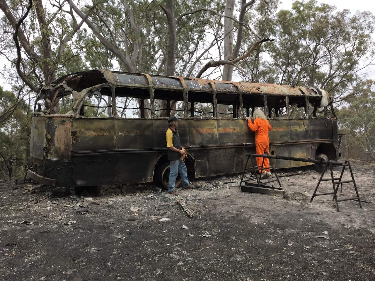 Daniel Kelly (orange) and Mathew Fowler next to Mr Kelly's burnt out heritage bus on his property at Lobethal in the Adelaide Hills, Adelaide, Saturday.