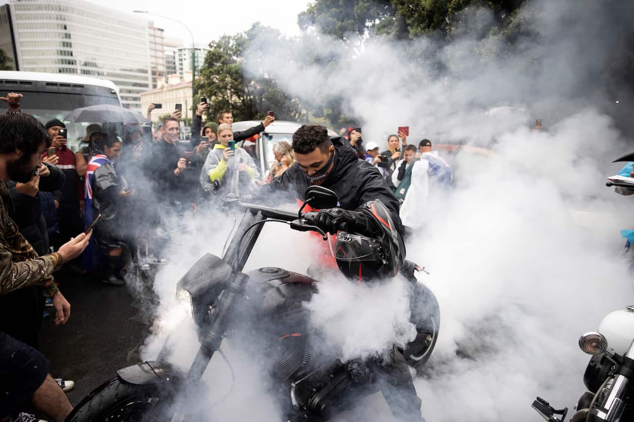 Protesters watch as a man spins the tire on his motorcycle in wet conditions as they demonstrate their opposition to coronavirus vaccine mandates at Parliament in Wellington, New Zealand, Saturday, Feb. 12, 2022. 