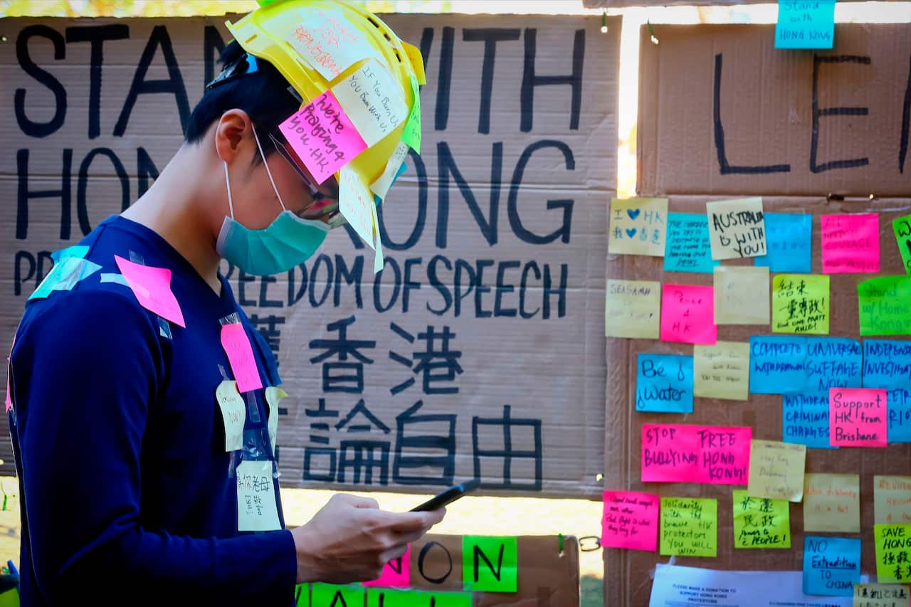 A supporter of the Hong Kong pro-democracy protests, seen covered in sticky notes, standing in front of makeshift "Lennon Wall" at the University of Queensland.