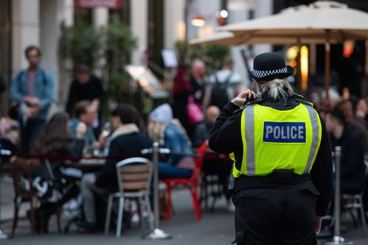 Police monitor people seated outside bars and restaurants in Soho, London, on the first day after the city was put into Tier 2 restrictions