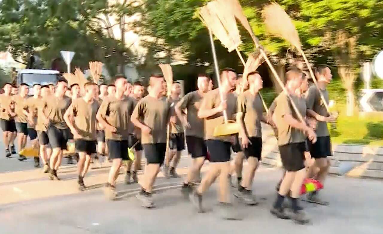 In this image made from video, Peoples Liberation Army soldiers, with brooms, arrive to clean up the protest area at Hong Kong Baptist University.