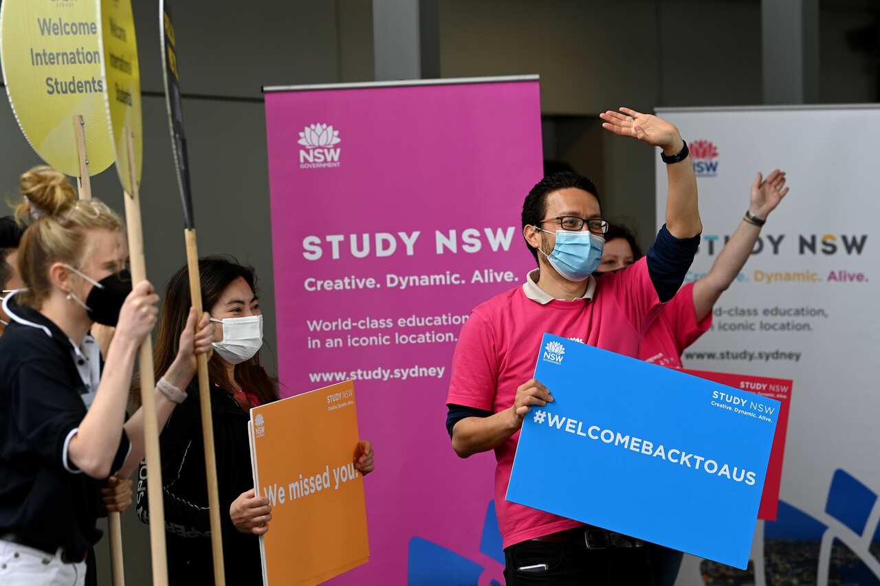 People hold signs NSW Government signs welcoming international students at Sydney airport in December, 2021.