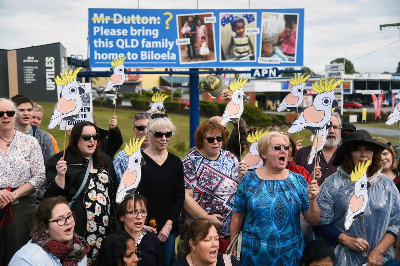 A group of around 100 friends and supporters of the family stand underneath a billboard for the campaign in Brisbane.