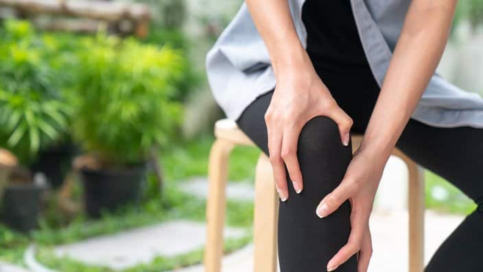 Young woman suffering from pain in knee, close up