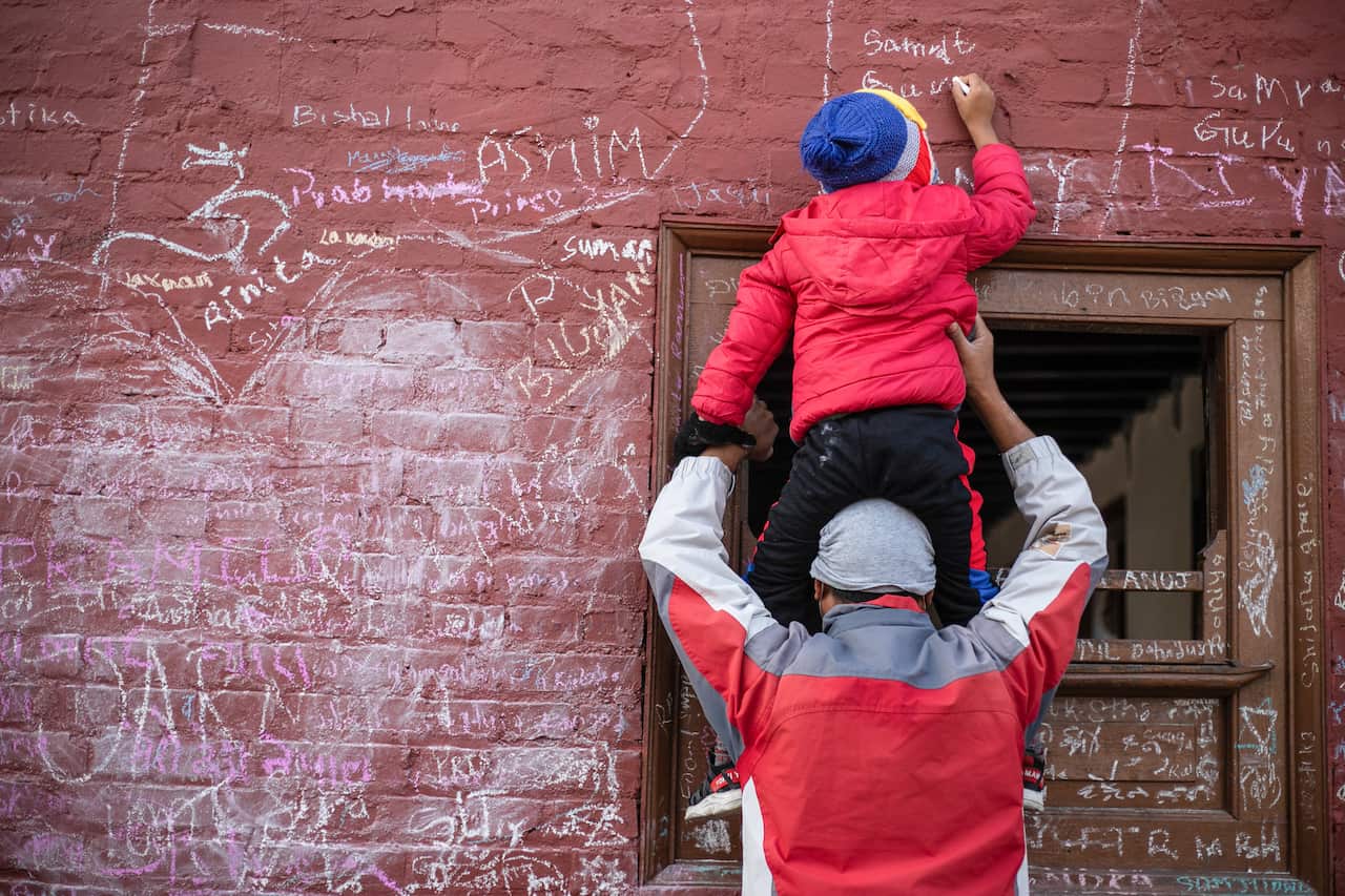 A parent helps his kid write on the walls of Saraswati temple during Shreepanchami, or Saraswati Puja in Nepal.