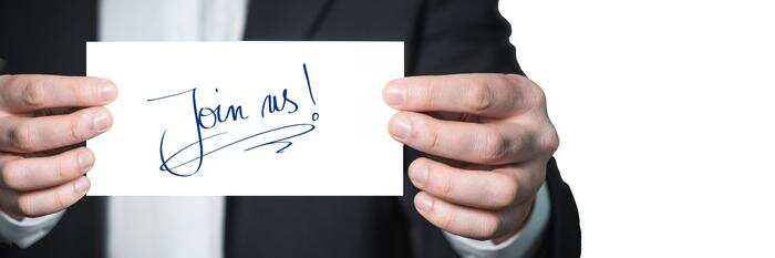 Image of a person holding a hand-written note saying 'Join us!'