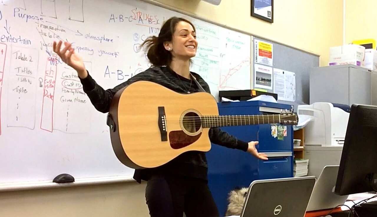 Teacher holding guitar performing a song in class