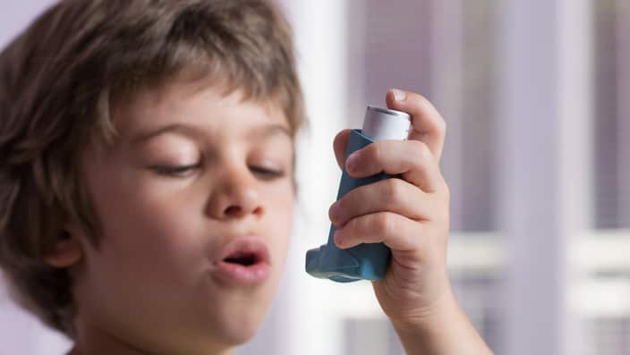 Boy using asthma inhaler to treat inflammatory disease, wheezing, coughing, chest tightness and shortness of breath. Allergy treating concept. Selective focus on inhaler.