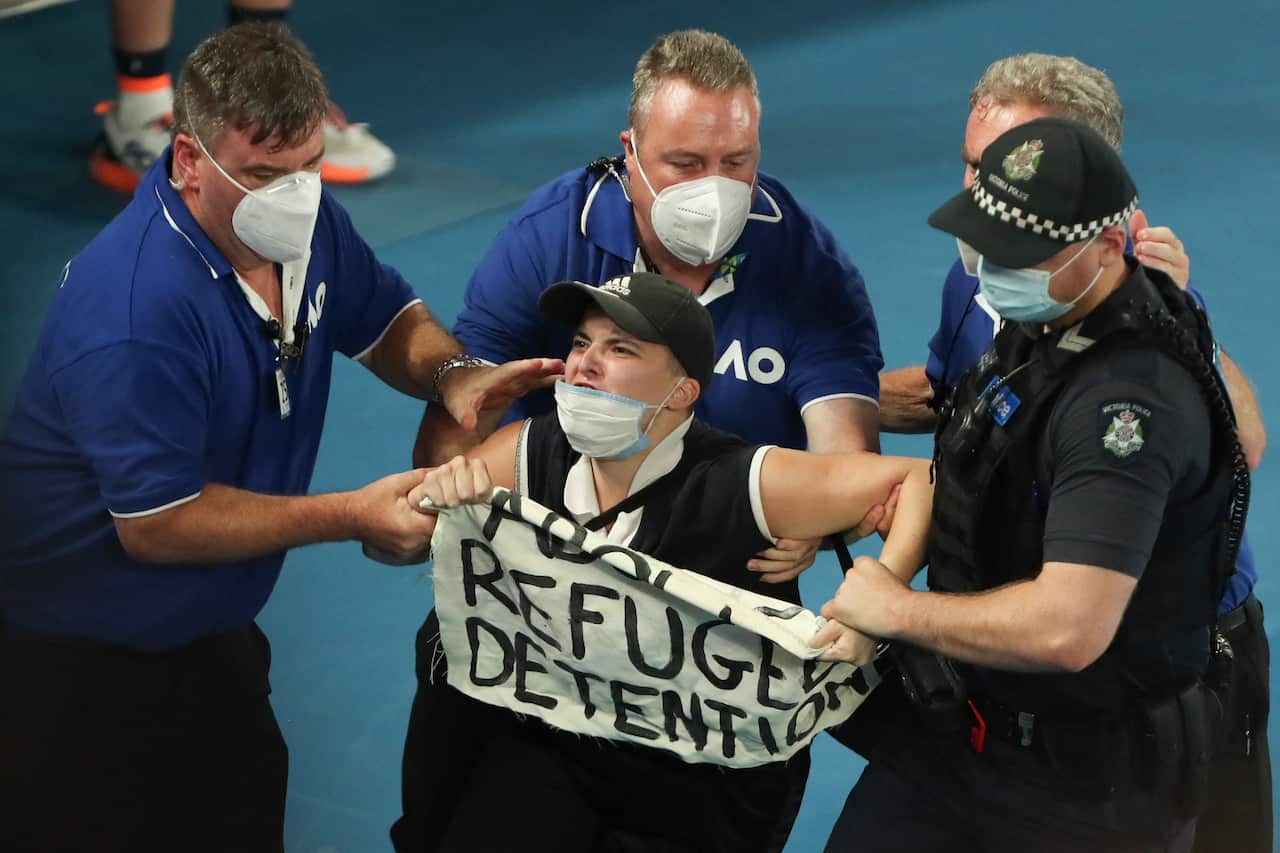 A refugee rights activist is detained by security after jumping onto the court during the men's singles final match