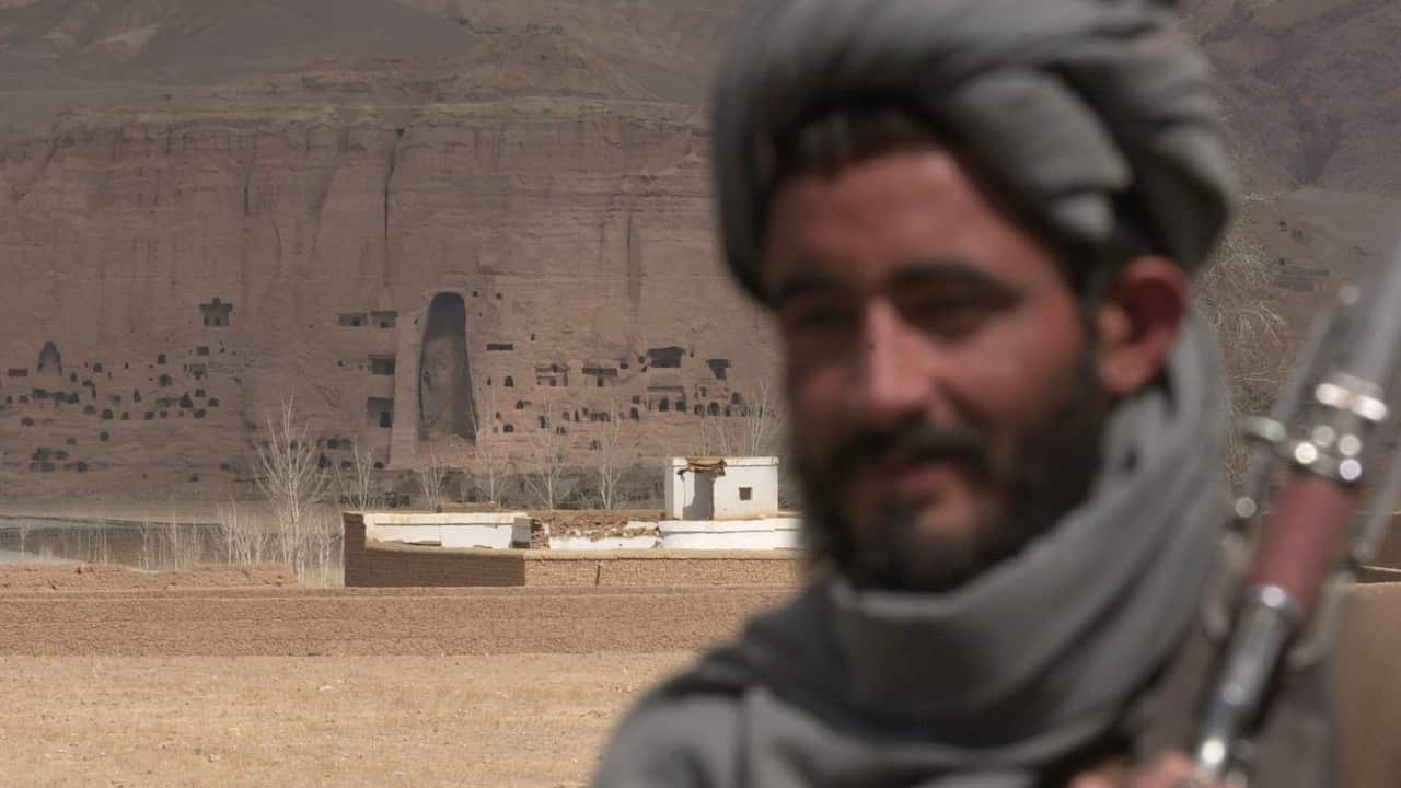 Empty shell of the 36-meter (120-foot) demolished Buddha statue is seen at center behind a Taliban soldier Monday, March 26, 2001 in Bamiyan, Afghanistan. 