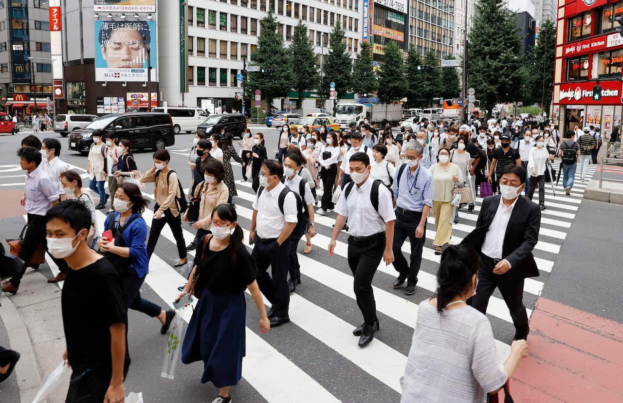 People wearing face masks to help curb the spread of the new coronavirus walk across a street in Tokyo, Japan, Wednesday, July 29, 2020. As Japan battles a surge in coronavirus cases, some areas may be running out of isolation facilities to monitor infect