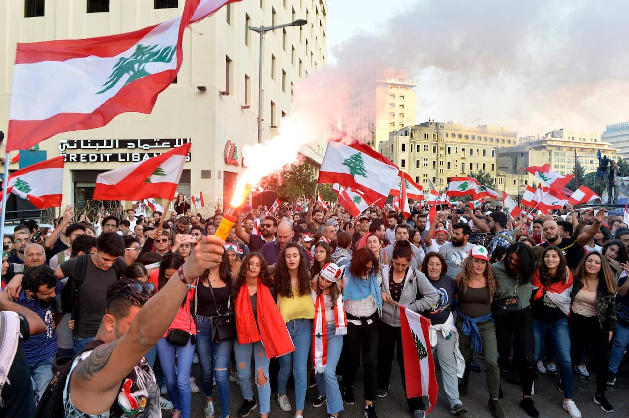 A protester lights a flare as other protesters carry Lebanese flags and dance during ongoing anti-government protests in downtown Beirut in 2019. 