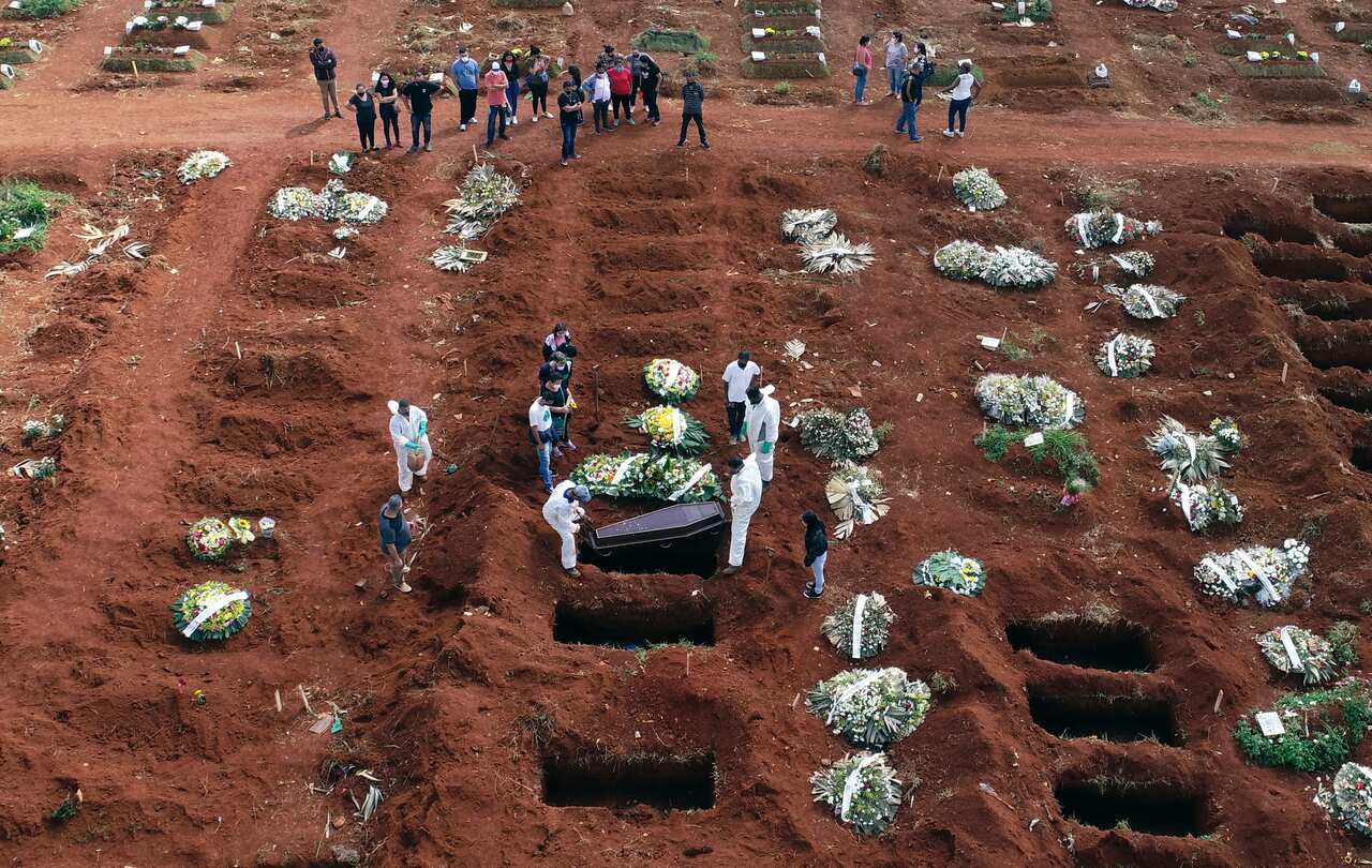 Cemetery workers wearing protective gear lower the coffin of a person who died from complications related to COVID-19 into a gravesite.