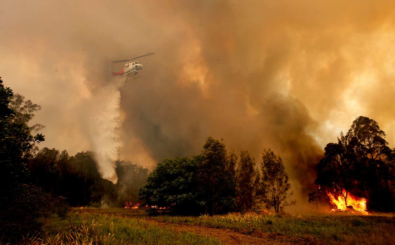 A fire bombing helicopter works to contain a bushfire along Old Bar road in Old Bar.