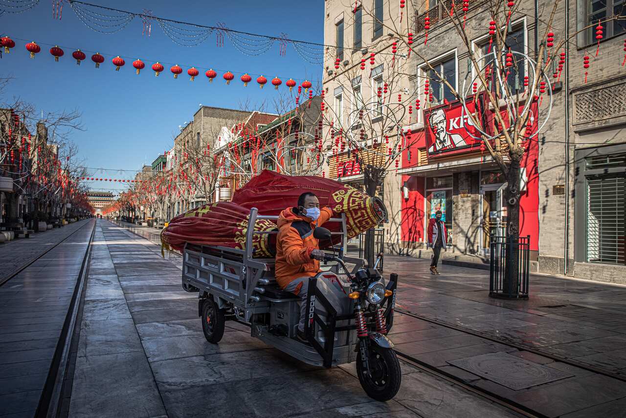 A worker wearing a protective face mask rides a three-wheeled vehicle on an almost empty pedestrian shopping street named Qianmen, in Beijing, China.