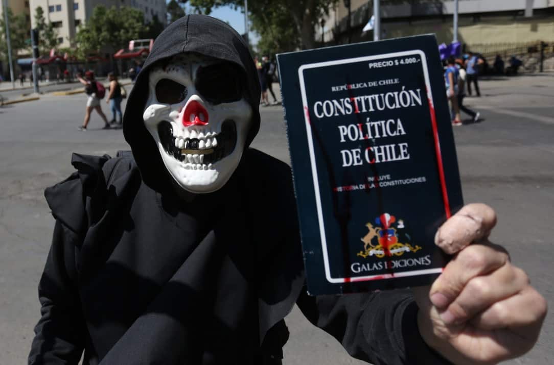 A man with a mask holds a Chilean constitution as demonstrators participate during a march at the Plaza Italia in Santiago, Chile, 18 October 2020. 