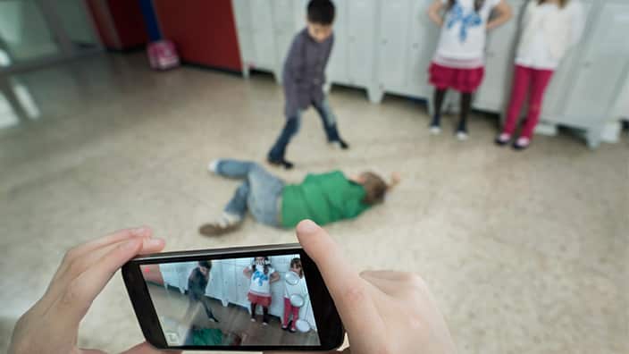 Persons hand filming two schoolboys fighting in school corridor with mobile phone