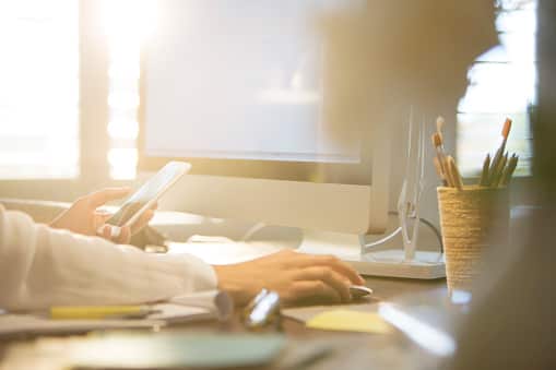 Woman using computer and texting on cell phone at desk