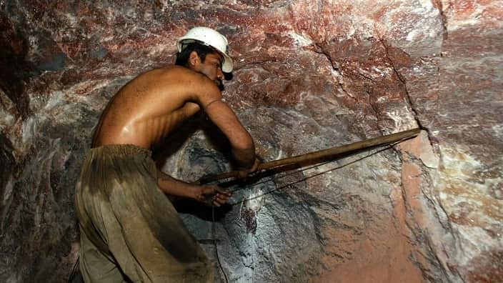 Laborers use hand drills and gunpowder to blast away the pink and orange-colored rock crystal.