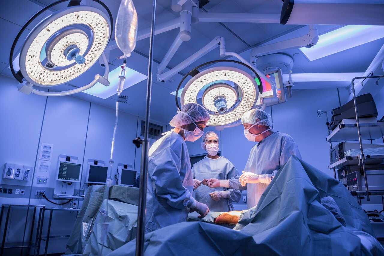 Surgeons operating on patient in operating theatre under lights