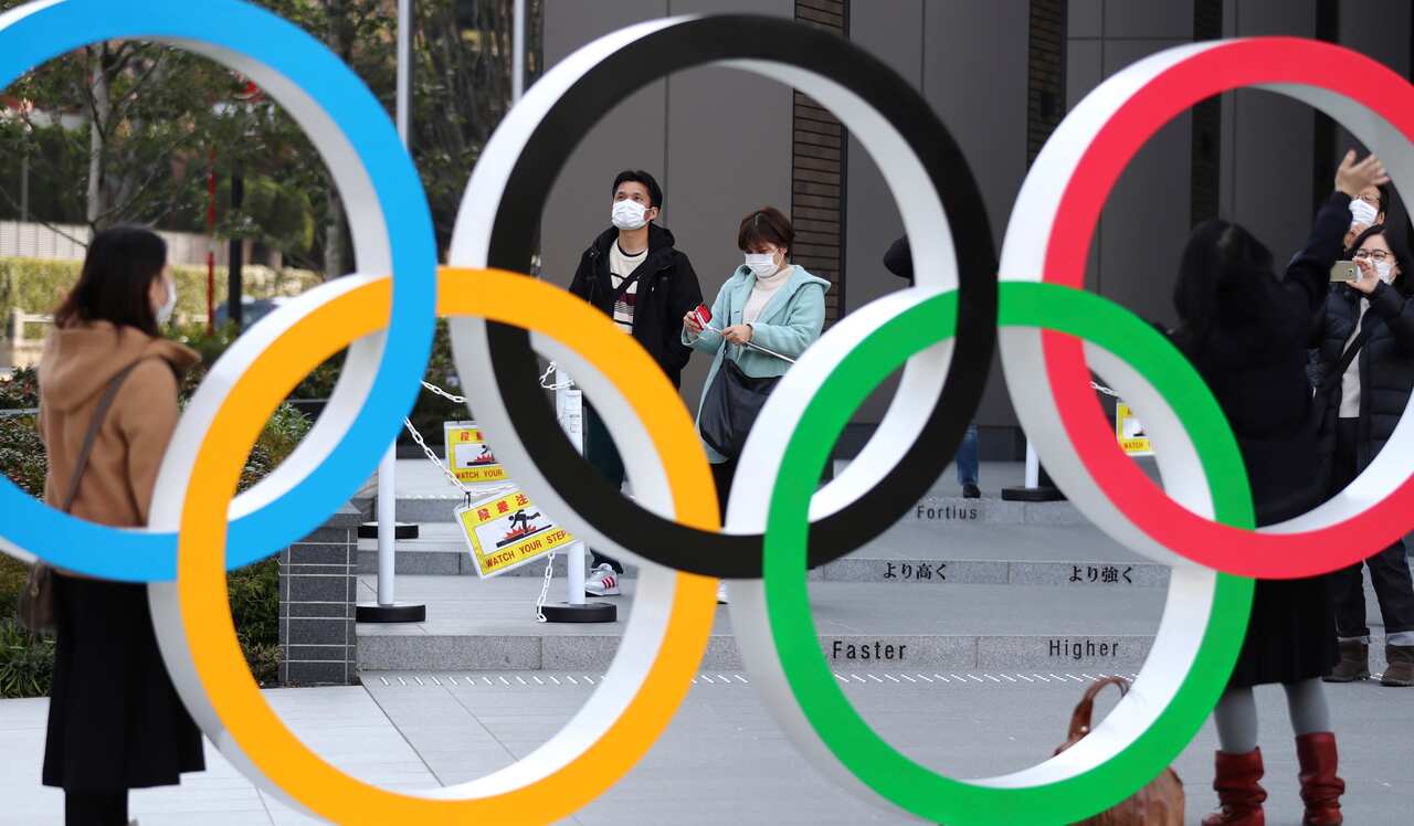 People wearing face masks walk by an Olympic rings installation at Japan Sport Olympic Square in Shinjuku, Tokyo.