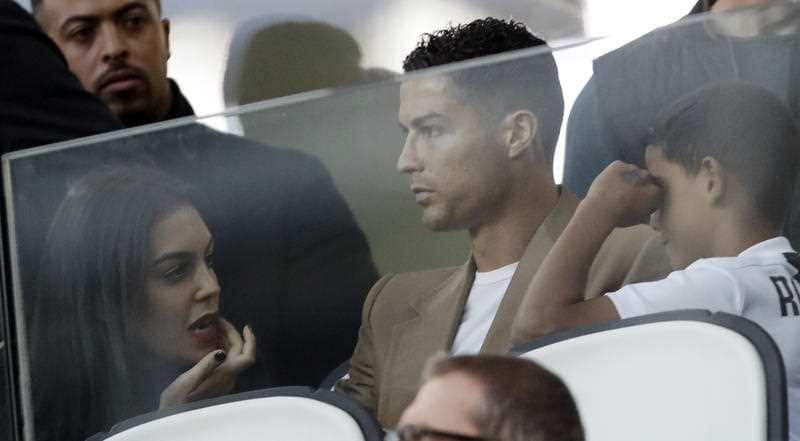 In this Tuesday, Oct. 2, 2018 filer, Juventus forward Cristiano Ronaldo, center, is flanked by his girlfriend Georgina, left, and his son Cristiano Jr, as he sits in the stands during a Champions League, group H soccer match between Juventus and Young Bo