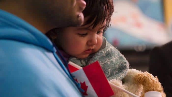 A young Syrian refugee is held by her father as they arrive at the Welcome Centre at Toronto's Pearson Airport on Friday, Dec. 18, 2015. (Chris Young/The Canadian Press via AP)