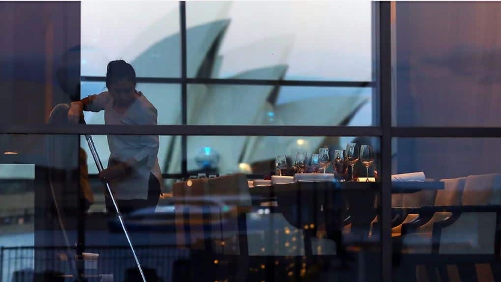 The Sydney Opera House can be seen in the reflection of a restaurant window as a worker uses a vacuum in Sydney 