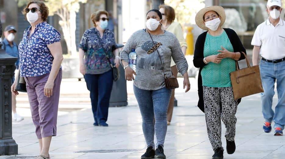 Pedestrians wearing facial masks walk along a street in Valencia, Spain.