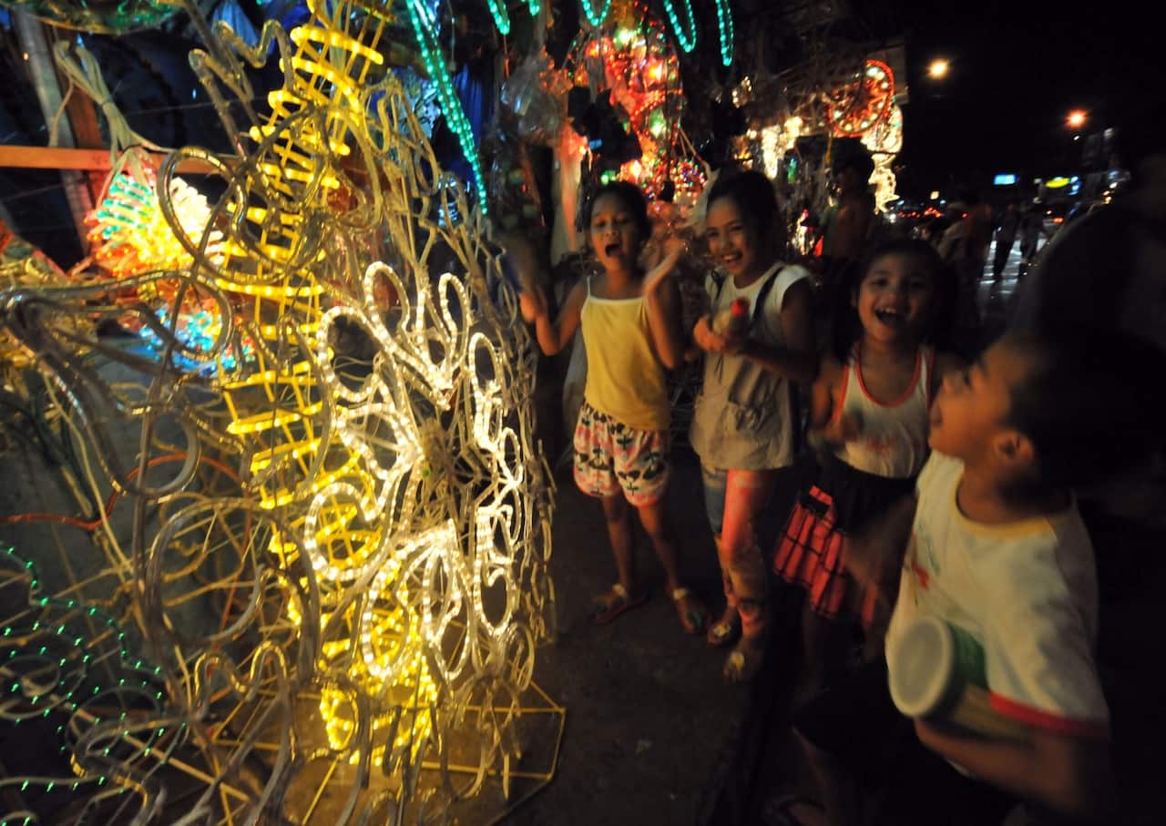children sing Christmas carols near lanterns on display, locally known as 'parol' along a street in Manila.