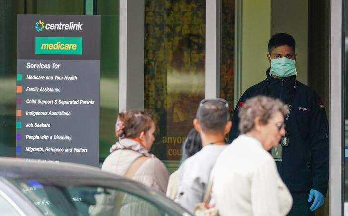 A security guard looks on as people are seen in long queue outside a Centrelink office in Abbotsford, Melbourne, Monday, 23 March, 2020. 