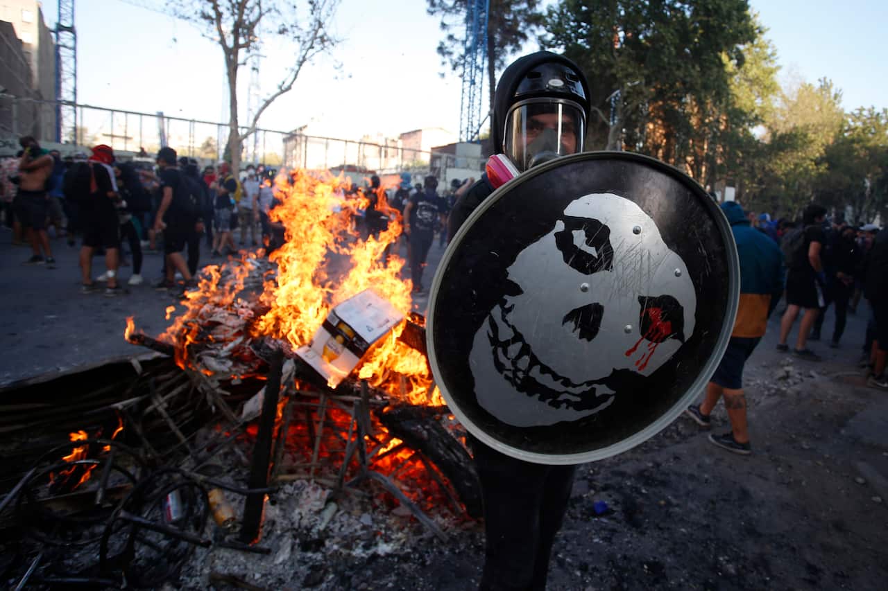 An anti-government protester stand in front of a burning barricade in Santiago.