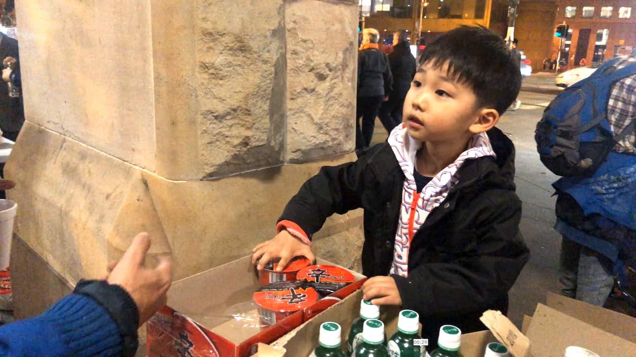 A child volunteer handing out a noodle cup to people in the line. 