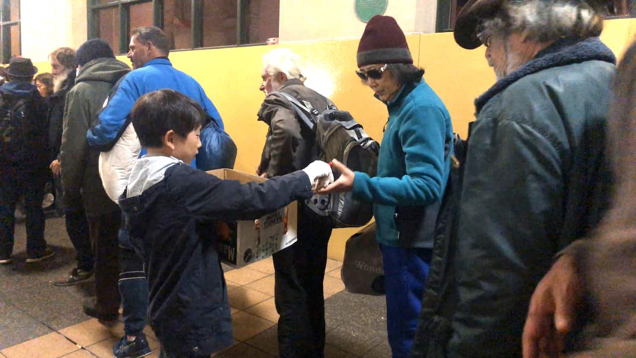 A child volunteer handing out fruit to people in the line. 