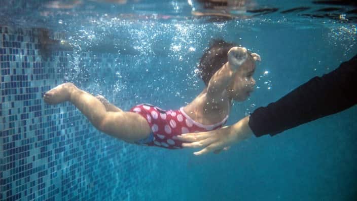 A mother submerges her child during a swimming lesson